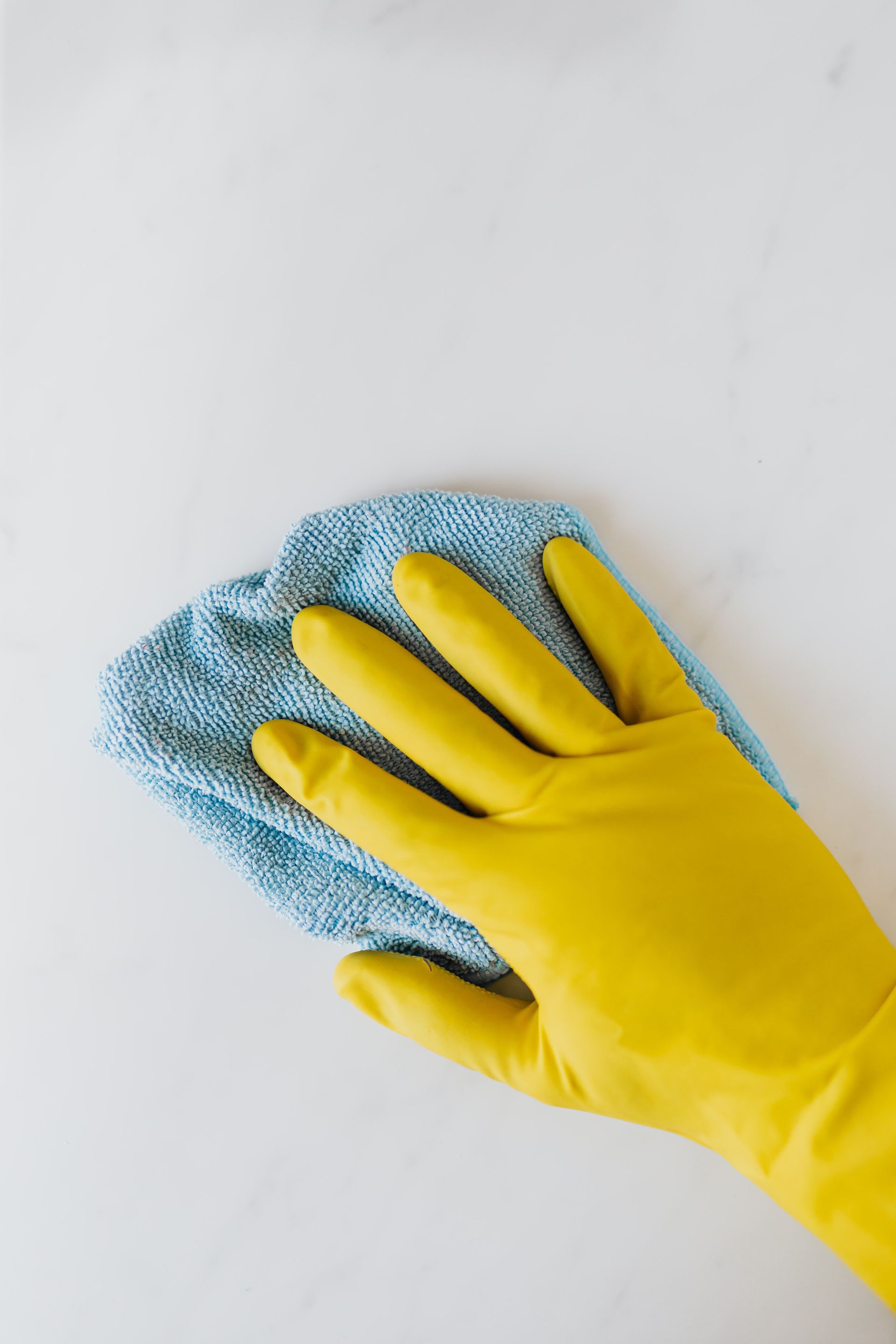 Top view of crop anonymous housekeeper in protective gloves cleaning and polishing white surface with blue rag